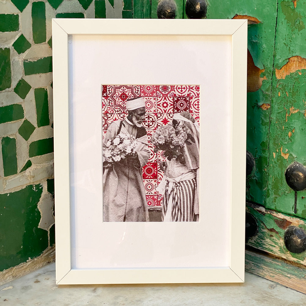 Tableau décoratif représentant un vieux couple marocain portant deux bouquets de fleurs, sur un fond de zellige marocain rouges, encadré dans un cadre blanc - Format A4.