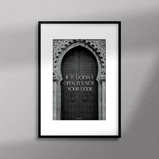 Tableau décoratif en noir et blanc d'une porte marocaine, avec la citation motivante : "If it doesn’t open it’s not your door", encadré dans un cadre noir - Format A3.
