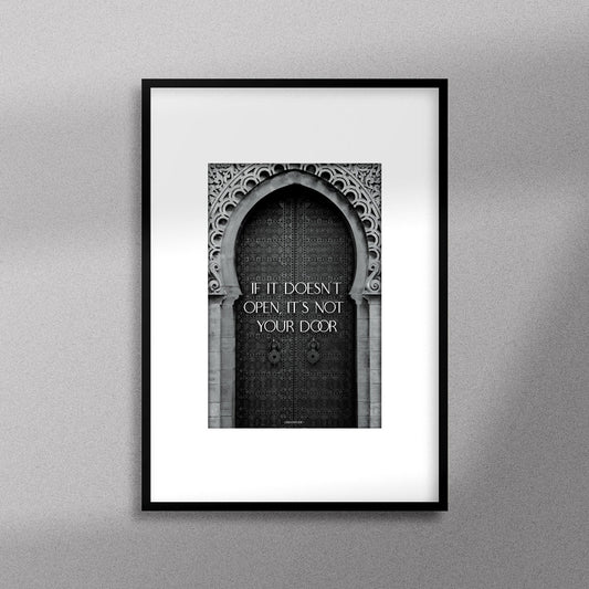 Tableau décoratif en noir et blanc d'une porte marocaine, avec la citation motivante : "If it doesn’t open it’s not your door", encadré dans un cadre noir - Format A4.